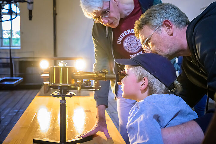 Kleiner Bub und Erwachsener schauen durch ein historisches Teleskop